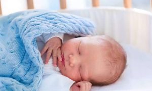 Peaceful newborn baby sleeping soundly under a blue blanket in a comfortable baby bassinet.