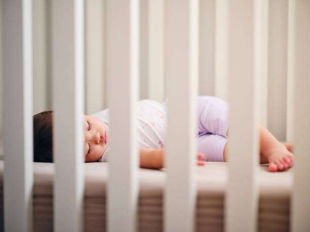 Peaceful baby sleeping soundly on their side in a secure white baby bassinet.