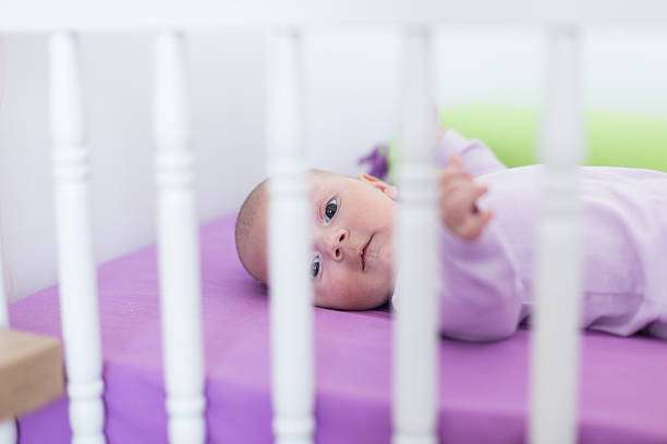 Adorable baby lies on a purple sheet in a cozy white baby bassinet.